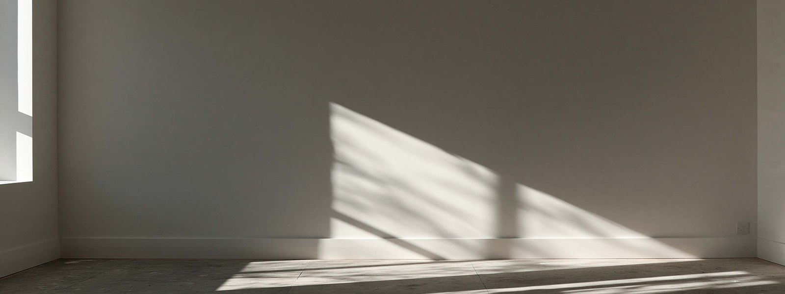 A wide finished wall with a sharp wedge of sunlight across it, the surface reading dead flat behind the light