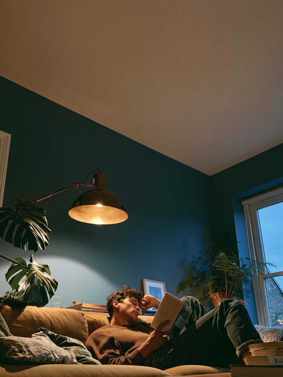 A man reading on a sofa under a smooth, evenly finished ceiling in a lamplit room