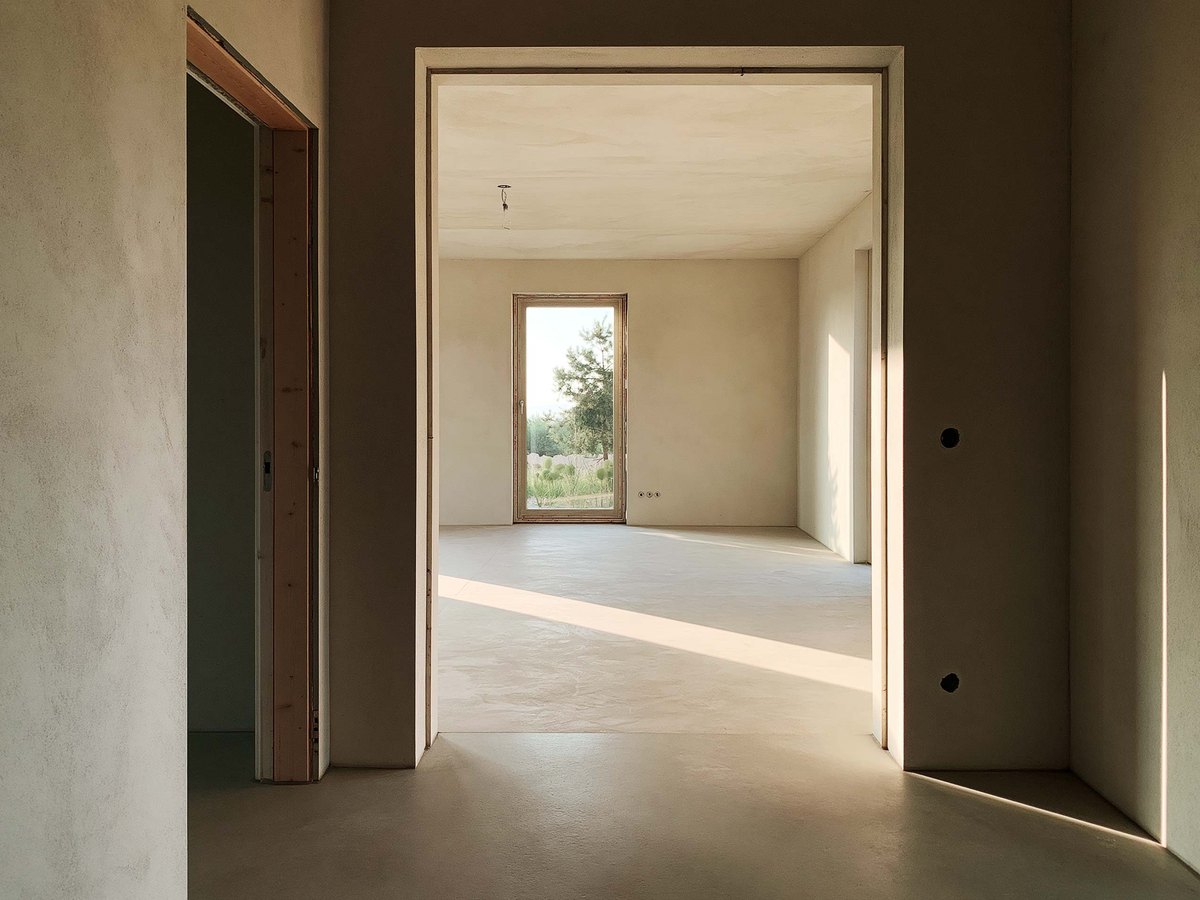 Looking through a doorway into a newly finished empty room, sunlight lying across the floor toward a tall window