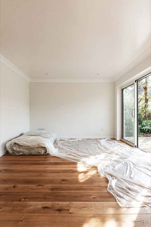 An emptied room with dust sheets across the floor under a smooth, scraped ceiling